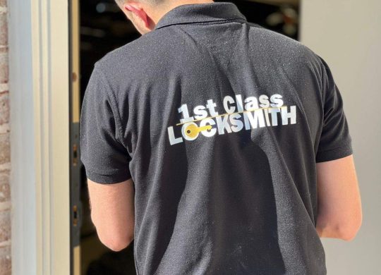 1st Class Locksmith Tech Securing a Home in Denton 1st Class Locksmith technician working on a residential door lock, wearing a black uniform with yellow company branding in Denton, TX
